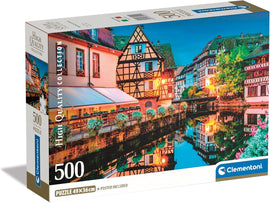 Clementoni Strasbourg Old Town 500-piece jigsaw puzzle packaging, featuring a vibrant scene of traditional houses along a canal at dusk, showcasing intricate details and colors. The puzzle measures 49x36 cm and includes a poster.
