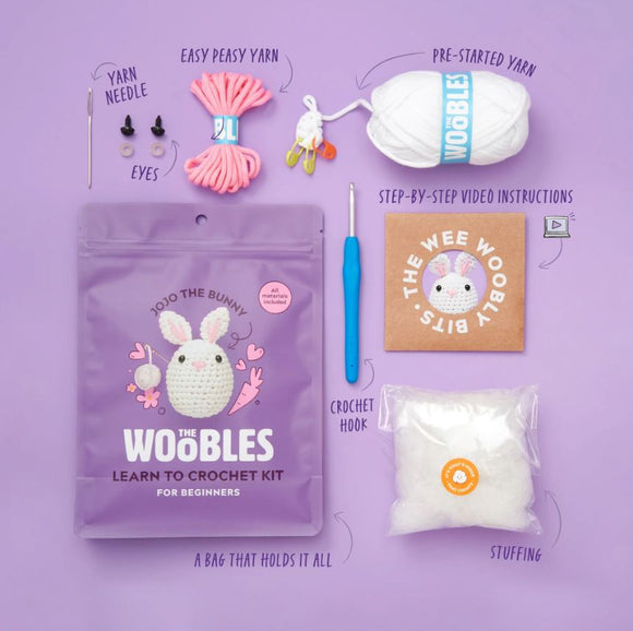 Jojo the Bunny Beginner Crochet kit by Woobles, featuring a colorful packaging with a cute bunny design. The kit includes easy peasy yarn, a crochet hook, yarn needle, eyes for the bunny, pre-started yarn, stuffing, and step-by-step video instructions, all neatly arranged on a purple background.