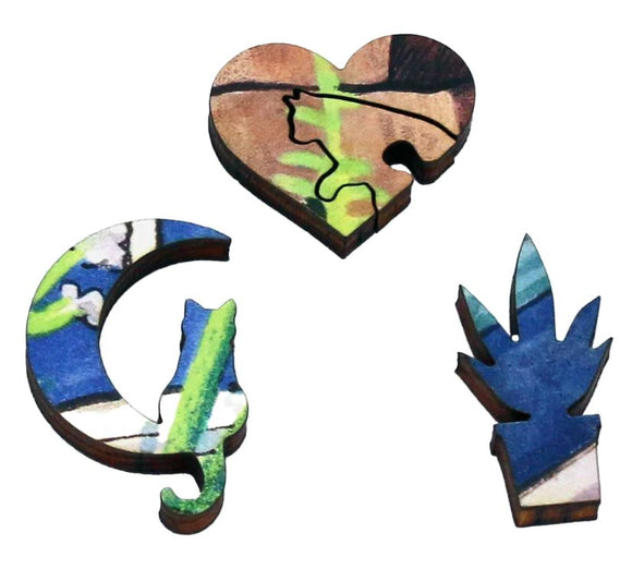 A close-up of three unique wooden jigsaw puzzle pieces featuring vibrant colors and intricate designs. One piece is shaped like a cat sitting, another like a heart with a cat outline, and the third resembling a potted plant. These pieces showcase the artistic details characteristic of the 'Cat In Garden' puzzle by Samuel Haywar.