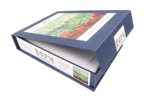 A closed jigsaw puzzle box titled 'Morning Rays' by Lisa Graa Jens, produced by Artifact Wooden Puzzles. The box features vibrant artwork on the top, depicting a colorful nature scene, showcasing vibrant greens, blues, and warm reds. The box is elegantly designed with a textured finish and includes identifying labels with the product name and other details.