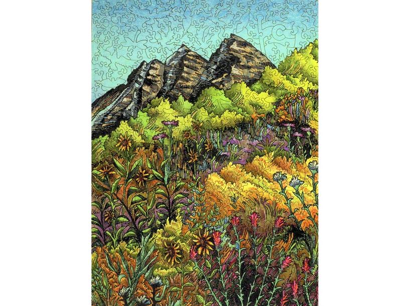 The Maroon Bells jigsaw puzzle by Liberty Puzzles features a detailed illustration of vibrant wildflowers in a variety of colors, set against a backdrop of the iconic Maroon Bells mountain peaks under a clear blue sky. The intricate design showcases diverse flora, with shades of green, yellow, purple, and orange, inviting puzzle enthusiasts to immerse themselves in this scenic outdoor representation.