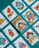 A vibrant display of Paper Royals Playing Cards by RunIt Decks, showcasing an array of colorful and whimsical illustrated cards. The deck is centered in the image, featuring a playful design with cartoon characters representing royalty. Surrounding the deck are several face cards, each adorned with unique illustrations that highlight a whimsical theme, set against a teal background.