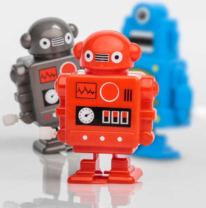 A set of colorful wind-up robots featuring a bright red robot in the foreground with a clock and heartbeat design on its chest. In the background, a gray robot and a blue robot are also visible. The robots have a vintage design with large, friendly eyes and movable limbs, perfect for fun and interactive play.