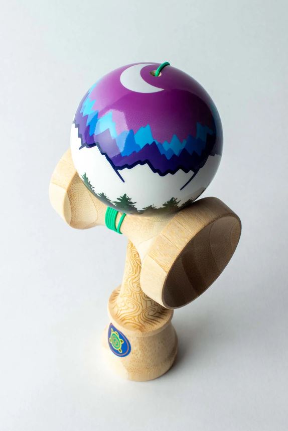 Moon Pro Model Joshua Flow Gro by Sweets Kendamas featuring a colorful ball with a mountain and moon design. The ken is made of natural wood with a smooth finish, showcasing a playful and artistic look. Perfect for skill-building and fun.