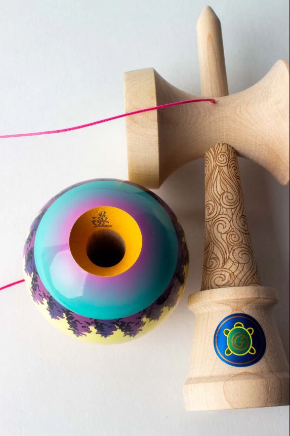 SUN Pro Model Joshua Flow Grov by Sweets Kendamas. The image features a colorful kendama with a glossy sphere top and intricately designed wooden handle, showcasing its vibrant purple, blue, and yellow patterns. The string is attached to the ball, ready for play.
