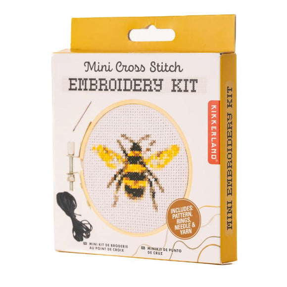 Kikkerland Bee Mini Cross Stitch Embroidery Kit packaging featuring a colorful bee design. The box includes a pattern, embroidery rings, a needle, and yarn for DIY crafting. Ideal for enthusiasts of cross stitch and needlework.