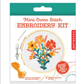 Kikkerland Flowers Mini Cross Stitch Embroidery Kit packaging featuring a colorful floral design in a circular embroidery hoop. The kit includes a pattern, embroidery rings, needle, and vibrant yarn threads.