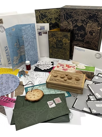 Threads of Fate by Postcurious is a captivating game kit featuring a beautifully designed box filled with various components. The arrangement includes decorative papers, maps, intricate puzzles, a wooden box with a unique control interface, colorful envelopes, and thematic artifacts that together create an immersive gameplay experience exploring storytelling and mystery.