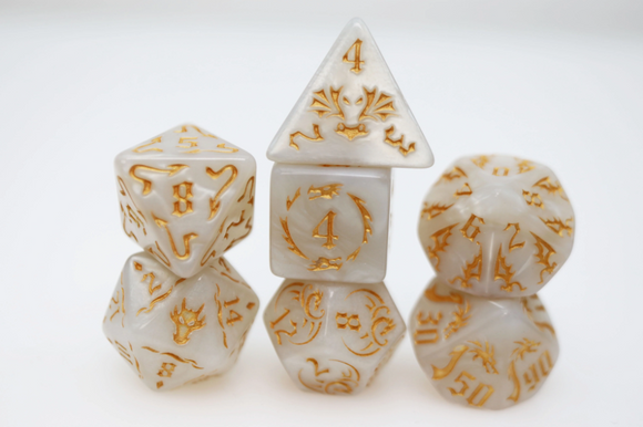 Drake's Flight RPG dice set by Foam Brain Games featuring intricately designed, translucent white dice with gold accents. The set includes various shapes, such as a d20, d10, and d4, each showcasing distinctive numeric and artistic embellishments, perfect for tabletop gaming enthusiasts and role-playing adventures.