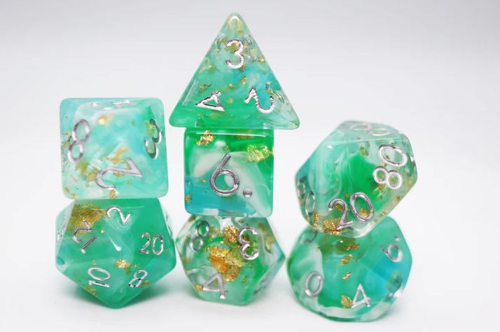 A set of colorful RPG dice from the Wealth of the Wild collection by Foam Brain Games. The dice feature a vibrant green color mixed with flecks of gold and have silver numbers displayed prominently on each face. The set includes various polygonal shapes commonly used in role-playing games.