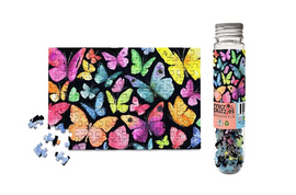 A colorful jigsaw puzzle featuring various butterflies in vibrant colors against a black background. The puzzle is partially completed with several pieces scattered nearby. The packaging shows a glass tube filled with small puzzle pieces, labeled with 'micropuzzle' and 'massive fun'.