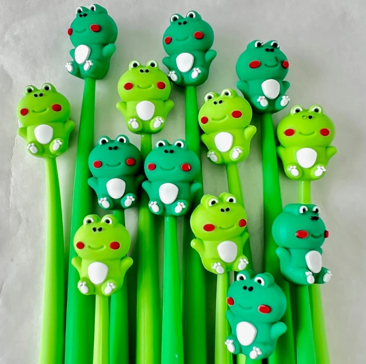 A collection of colorful Frog Wiggle Gel Pens by BC Mini, featuring various cute frog designs atop vibrant green pen bodies. Each pen has unique frog figures with cheerful expressions, making them ideal for kids and stationery lovers alike.