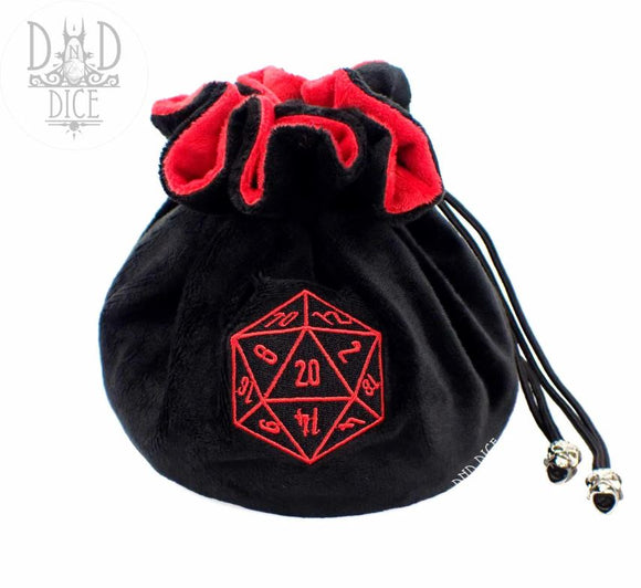 A cozy black fuzzy dice bag with a red velvet lining, featuring a stitched red d20 dice design on the front. The bag is cinched at the top with drawstrings, adorned with decorative silver accents. Perfect for holding gaming dice or other small items.