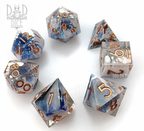 A set of seven beautifully crafted gravitational wave acrylic RPG dice by DND Dice. Each die features a unique blend of translucent blue and clear acrylic, accented with shimmering copper numbers for easy readability. The shapes include various polyhedral designs, ideal for tabletop gaming.