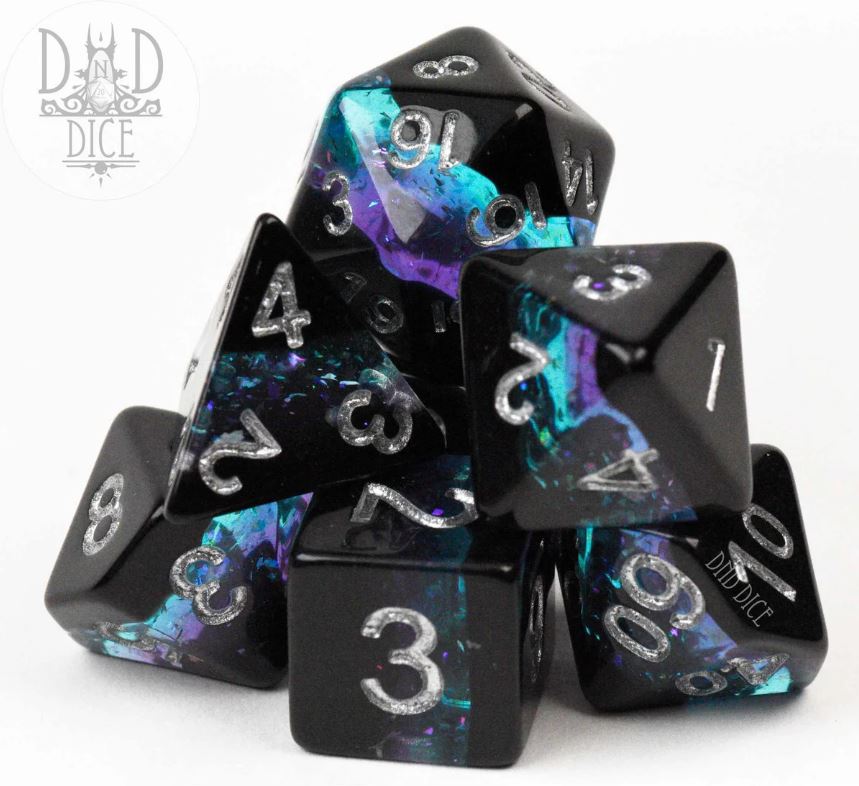 A close-up view of DND Dice's Crystalline Geode RPG Dice Set featuring a collection of unique, multi-faceted dice in shades of black, purple, and azure. The numbers are engraved and highlighted with silver for visibility. The dice are arranged in a stacked formation against a white background, showcasing their intricate design and sparkle.