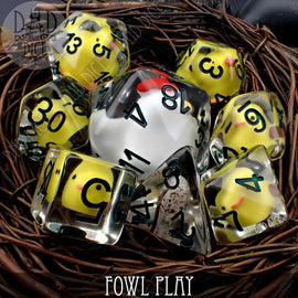 A colorful 8-piece RPG dice set titled 'Fowl Play' by DND Dice. The set includes various polyhedral dice, featuring yellow with black numbers and a transparent design with added playful motifs. All the dice are elegantly arranged in a circular formation surrounded by a natural twine or vine base, highlighting their vibrant colors and unique designs, perfect for tabletop gaming.