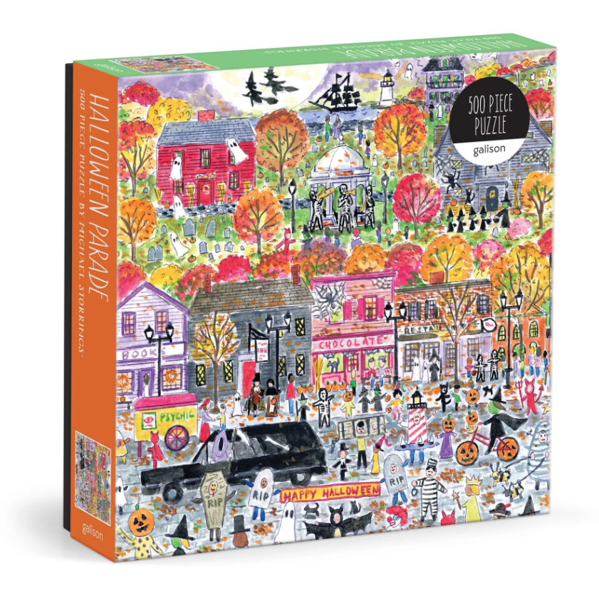 Halloween Parade jigsaw puzzle featuring a vibrant autumn scene with playful ghosts, decorated houses, and costumed characters celebrating Halloween. The design showcases a lively street scene filled with autumn trees, pumpkins, and festive shops, all rendered in a colorful and whimsical art style by Michael Storrings. The puzzle comes in a sturdy box and includes 500 intricate pieces for a fun challenge.