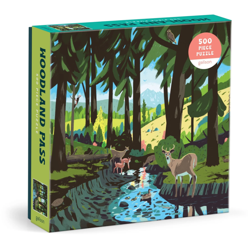 A colorful jigsaw puzzle box titled 'Woodland Pass' by Galison, featuring an illustration of a serene forest scene with trees, a stream, and wildlife including deer and ducks. The box indicates it contains 500 pieces.