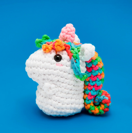 A colorful, knitted unicorn plush, named Rainbow Billy, showcasing vibrant yarn in various colors including pink, orange, and blue. The unicorn features a signature horn and adorable facial features, set against a blue background.