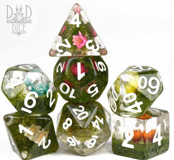 A vibrant set of seven RPG dice featuring a Prairie Flowers design. Each die is encased in transparent resin filled with miniature flowers and greenery, displaying clear white numbers for easy readability. The set includes a variety of shapes such as a D20, D12, D10, D8, D6, and D4, perfect for tabletop gaming enthusiasts.