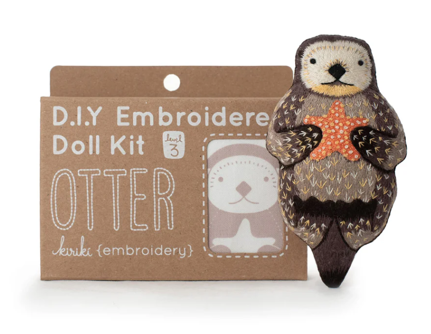 Otter Doll Embroidery Kit by Kiriki Press, featuring a cute otter holding a starfish. The kit is displayed in a brown cardboard packaging with playful graphics and the label indicating it's a level 3 DIY project.