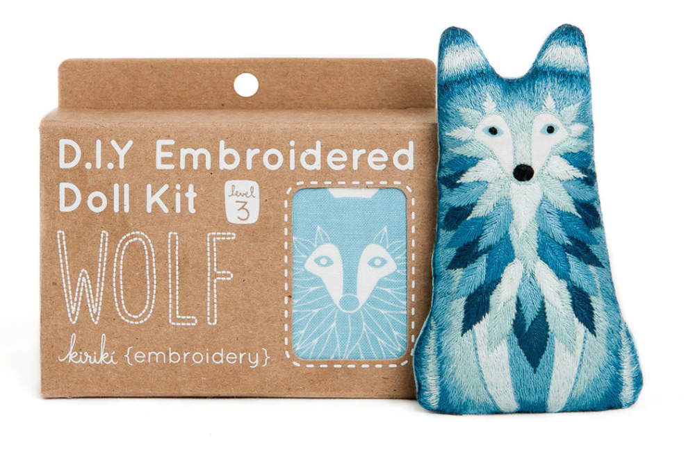 The Wolf Doll Embroidery Kit by Kiriki Press features an intricate embroidered doll in shades of blue and white, displaying a wolf design. The kit is presented in eco-friendly packaging with the title 'D.I.Y Embroidered Doll Kit' prominently displayed. It also indicates a difficulty level of 3, suitable for intermediate crafters, along with a graphic of the finished wolf doll. Perfect for DIY enthusiasts looking to create a unique decorative piece.