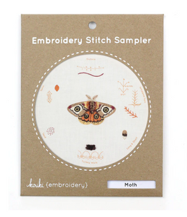 Moth Embroidery Stitch Sampler by Kiriki Press features a beautifully illustrated moth alongside various embroidery stitch guides. The design incorporates detailed illustrations and labels for each stitch type, all presented on a light fabric background, making it an ideal DIY kit for embroidery enthusiasts.