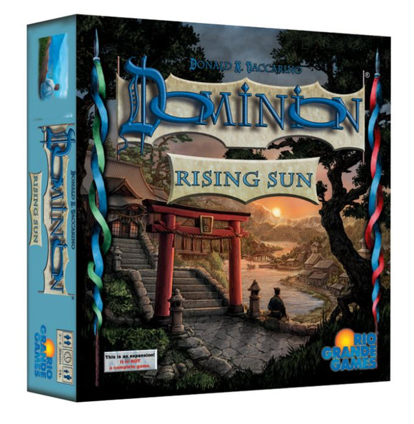 The game box for Dominion: Rising Sun by Rio Grande Games features a beautiful illustration of a serene landscape with a traditional Japanese gate, a river, and mountains at sunset. The title is prominently displayed in stylized blue letters, and the artwork reflects themes of strategy and adventure.