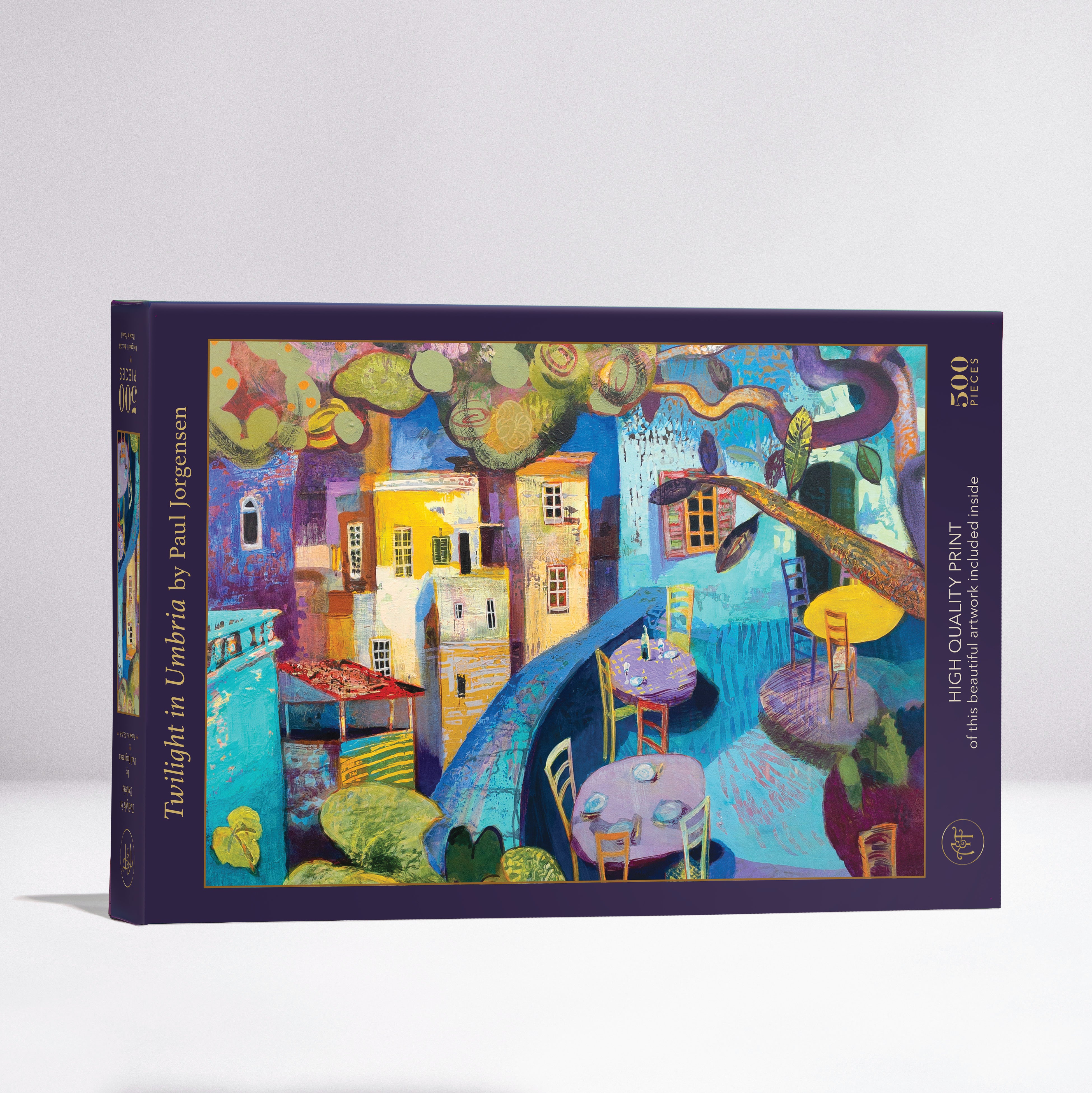 Twilight in Umbria jigsaw puzzle by Art & Fable Puzzle Co featuring a vibrant and colorful illustration of a quaint Italian village at twilight. The puzzle contains 500 pieces, showcasing a scene with bright buildings, lush greenery, and outdoor seating, perfect for puzzle enthusiasts.