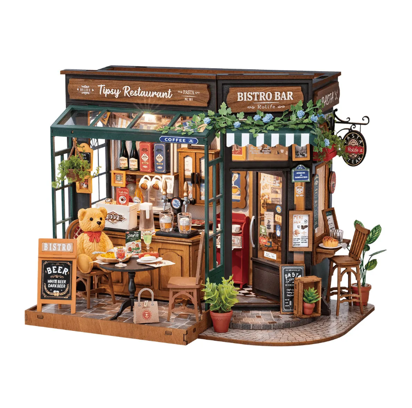 Tipsy Restaurant Model by Robotime, a detailed DIY kit showcasing a charming bistro scene. Features include miniature tables with a teddy bear, outdoor menu signage, delicious food items, and a cozy interior décor with plants and drinks, perfect for collectors and craft enthusiasts.