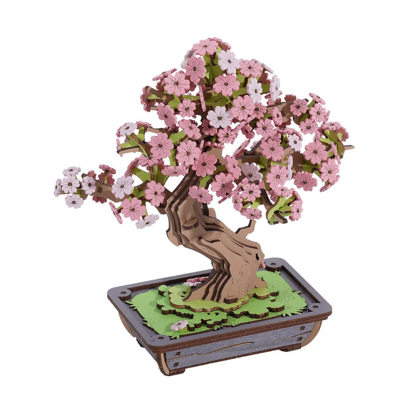 A beautifully crafted Sakura Bonsai model made by Robotime, featuring delicate pink and white cherry blossom flowers on a textured brown tree trunk, set on a green base.