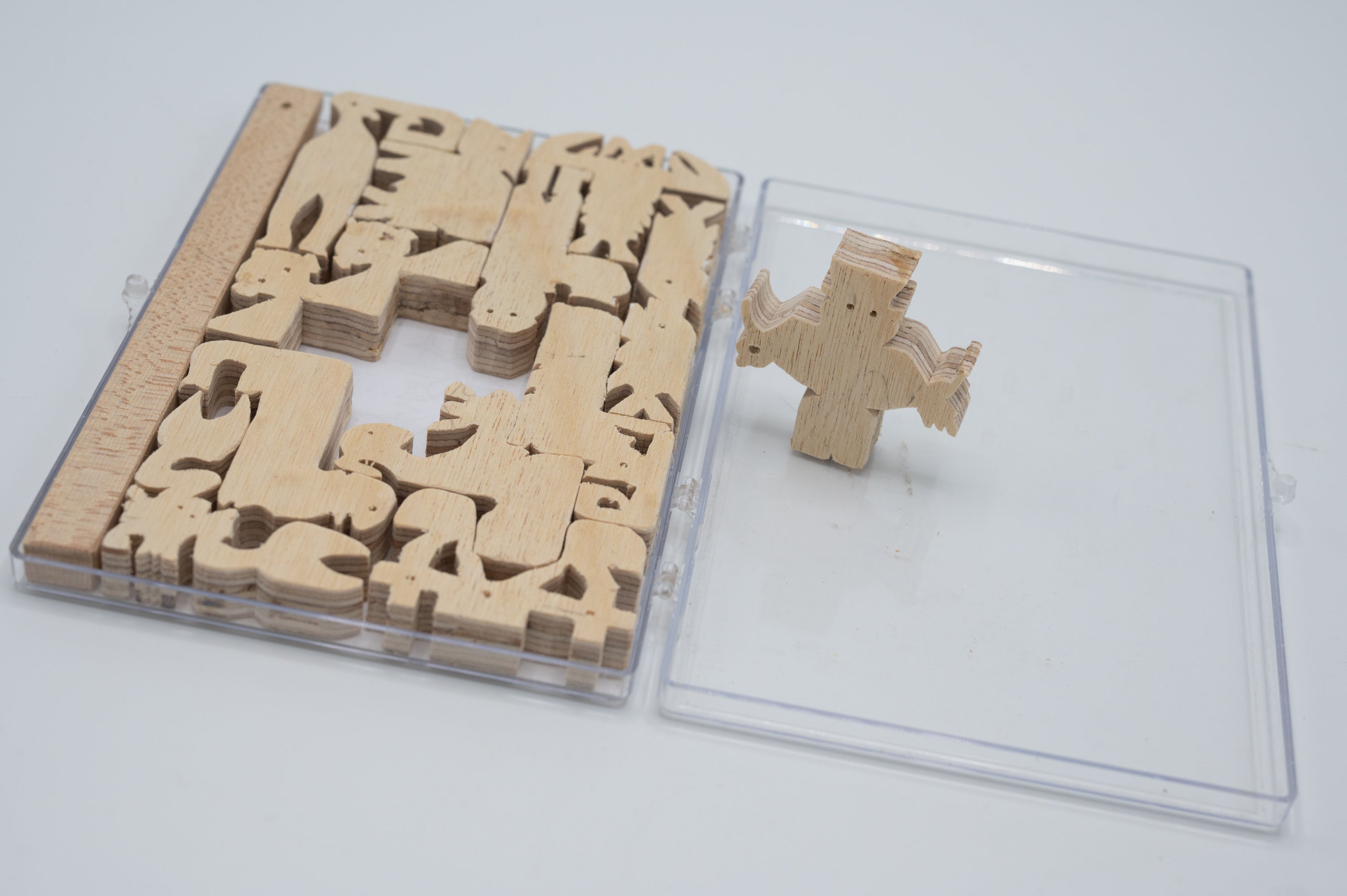 The Pentomino Piece Puzzle by Here to There Companies features intricately designed wooden pieces arranged in a clear case. It includes a unique shaped pentomino piece that stands out, showcasing the creative challenge it offers. Ideal for puzzle enthusiasts and designed for engaging play.