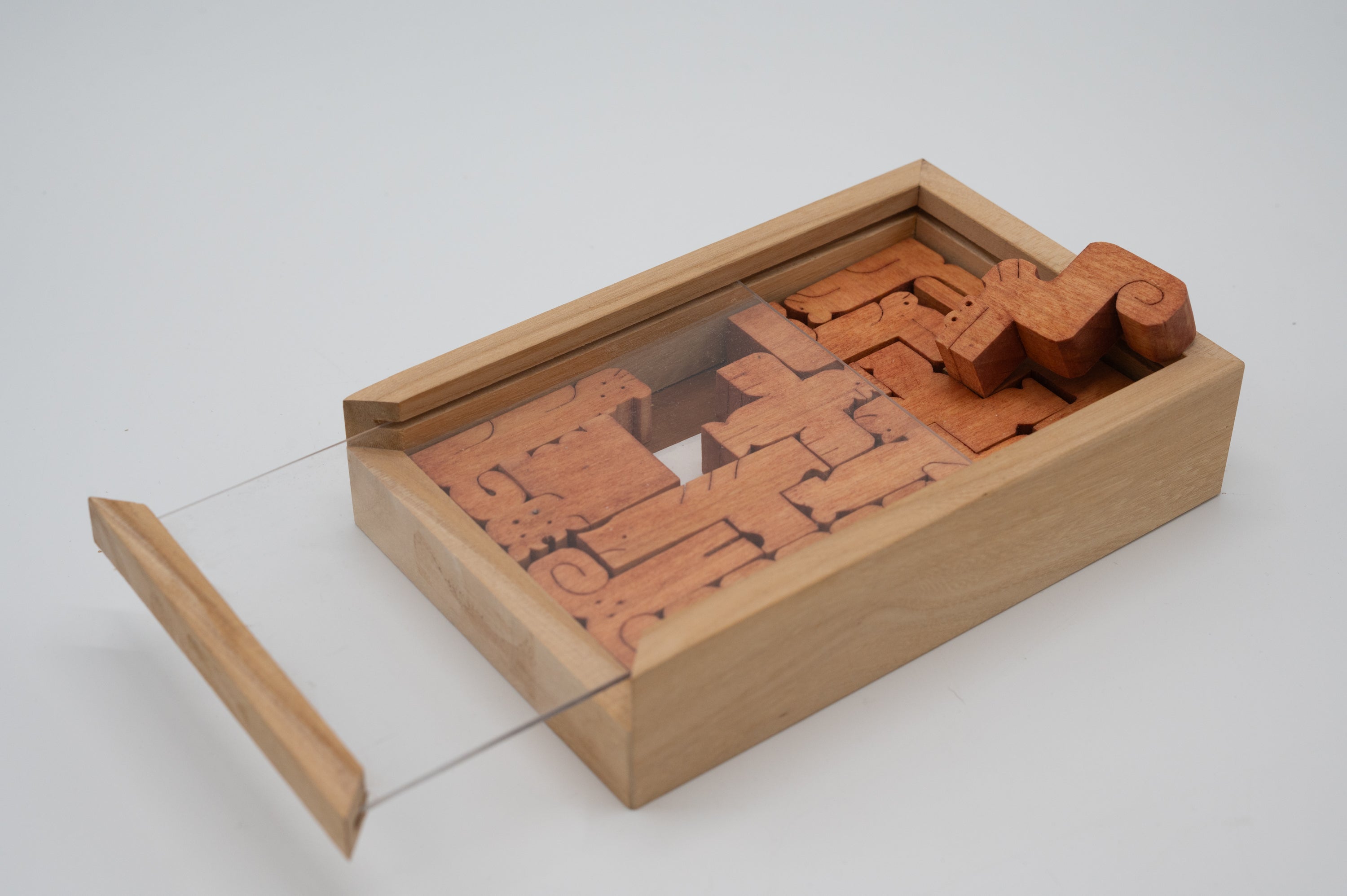 A wooden mechanical puzzle titled 'Signs of the Zodiac', designed by Saul Bobroff. The puzzle features intricately shaped pieces representing zodiac signs, beautifully crafted from wood and stored in a sleek, open wooden box with a transparent lid.