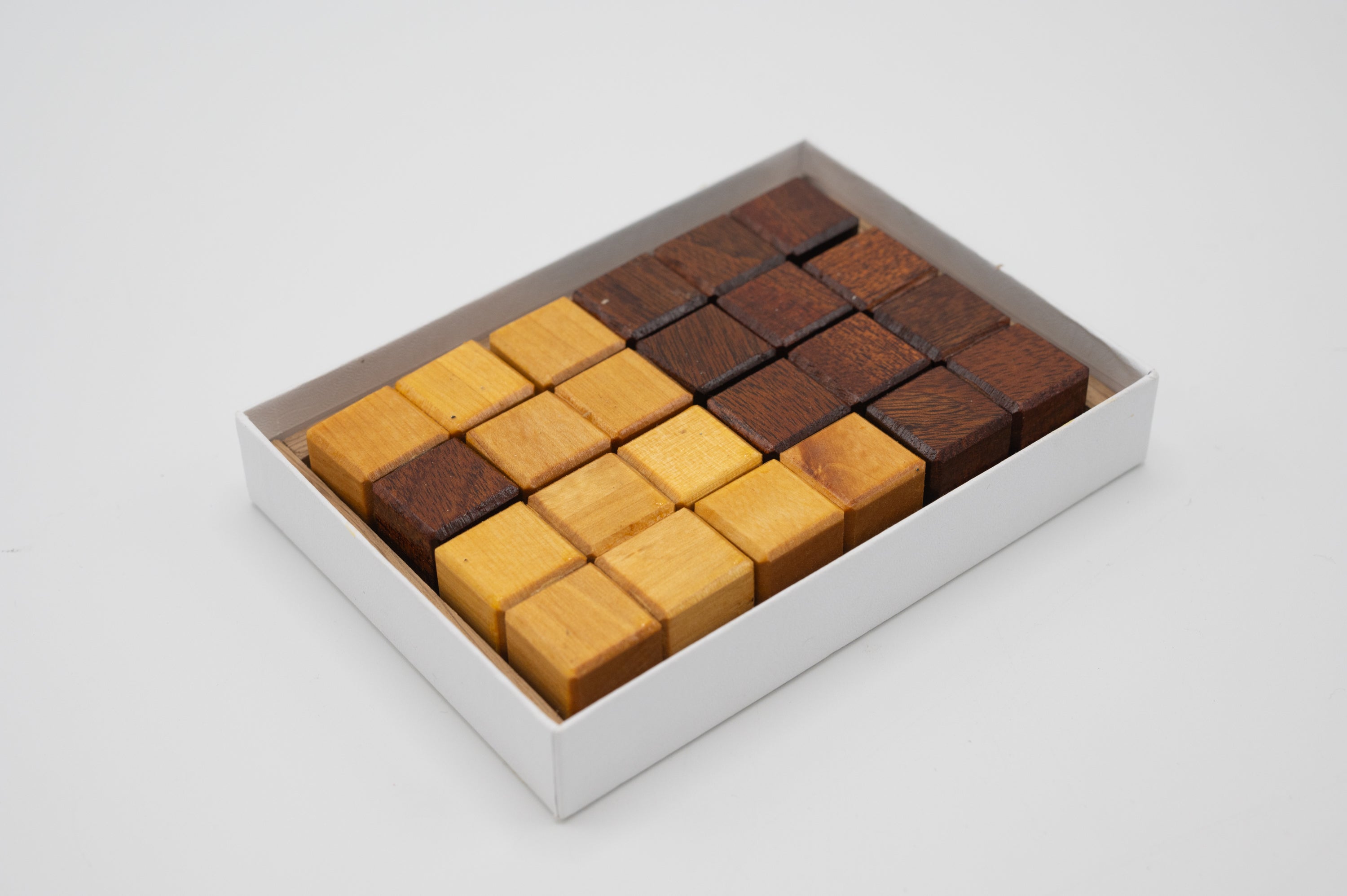 Half & Half by Saul Bobroff is a mechanical puzzle comprising a beautifully crafted set of wooden blocks in a 4x4 grid, featuring both light and dark wood tones. The puzzle challenges users to arrange the pieces in a way that explores spatial reasoning and problem-solving skills. It comes in a sleek, minimalistic white box for easy storage.