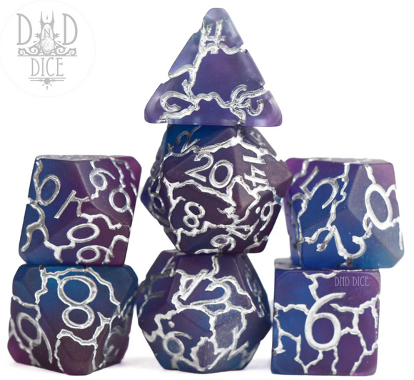 A set of 7 beautifully designed RPG dice from DND Dice named Chain Lightning. The dice feature a striking purple and blue color scheme with silver numbering and detailed lightning-like patterns. The set includes a variety of shapes commonly used for tabletop gaming, such as a D20, D12, D10, D8, D6, and D4, all stacked and displayed elegantly.