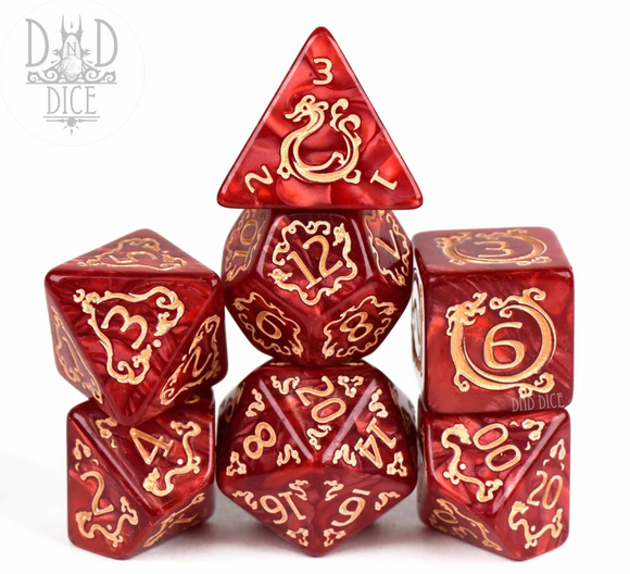 A set of seven beautifully crafted RPG dice with a vivid red color and gold numbering. The set includes a d20, d12, d10, d8, d6, d4, and a pyramidal d3, designed for tabletop gaming enthusiasts.