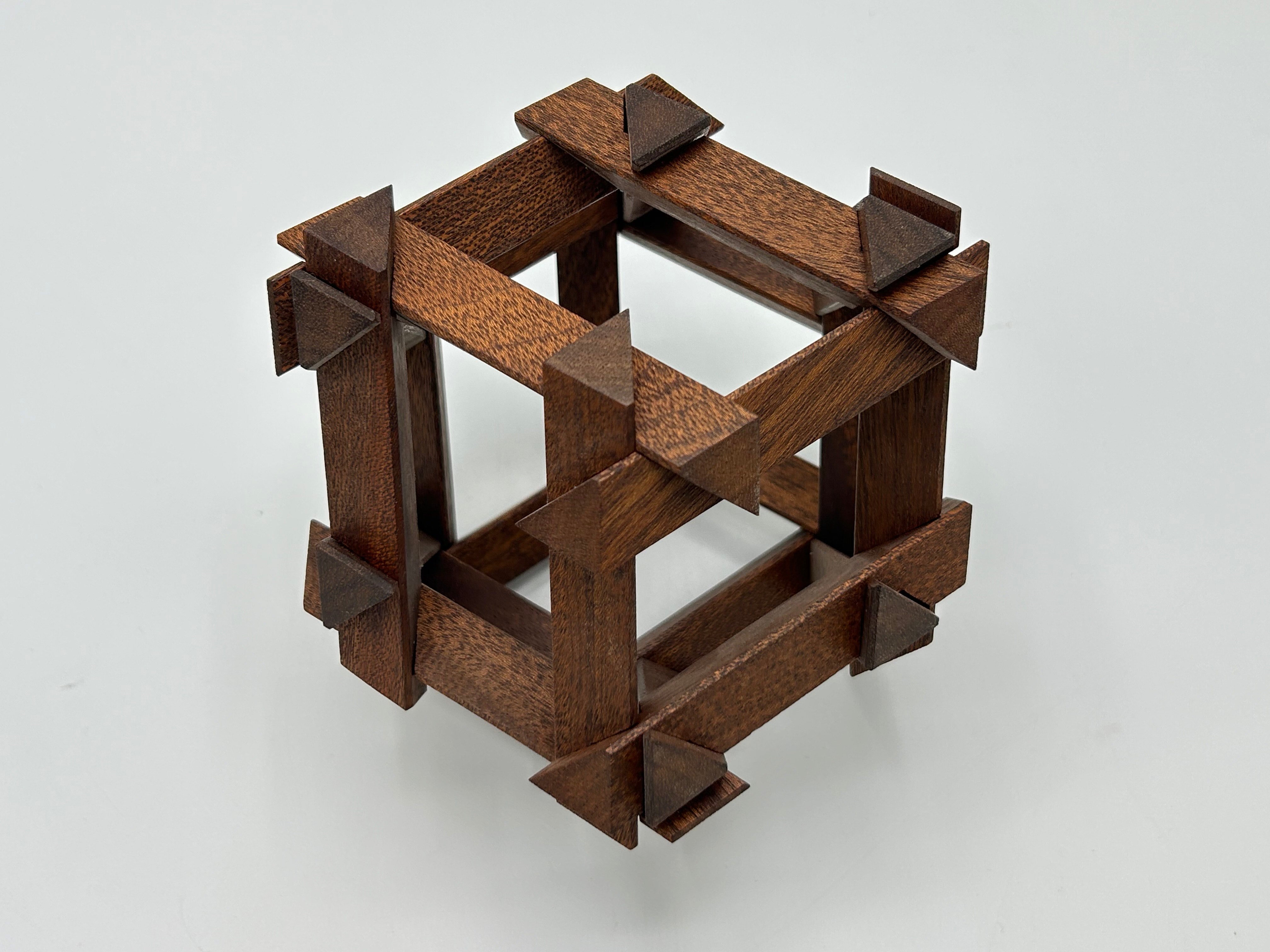 The RD Skeleton by Dubois is a beautifully crafted mechanical puzzle composed of intricately connected wooden pieces featuring a cubic design with angular accents. The puzzle is made from high-quality dark wood, lending it an elegant and sophisticated appearance. Each component showcases meticulous craftsmanship, providing both a challenge and a visually appealing decorative piece for puzzle enthusiasts.