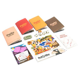 An assortment of game components from 'Parks: Roll & Hike' by Keymaster Games, including rulebooklets in various colors, a park guide, dice, and a colorful game board featuring scenic landscapes and hiking trails.