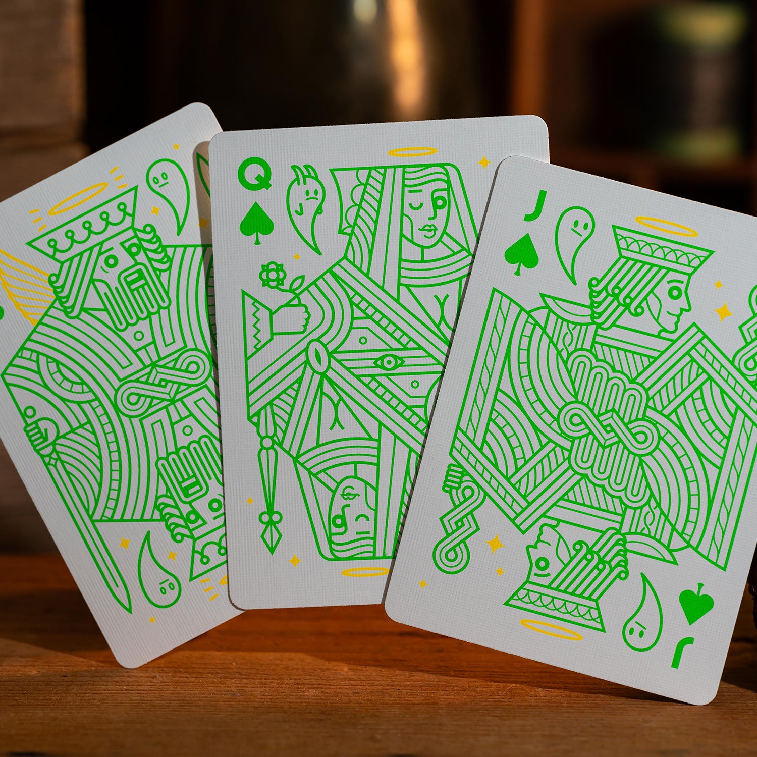 Three elegant Fantasma (Ectoplasm) playing cards by Thirdway Industries, featuring intricate green line art designs. The cards depict a king, queen, and jack, each adorned with ghostly elements and halo motifs, set against a textured background. Ideal for game enthusiasts seeking a unique addition to their collection.