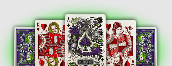 A set of Beetlejuice Playing Cards by Theory 11 featuring unique illustrations of characters and scenes from the classic film. The cards display vibrant colors, including green, red, and purple, showcasing artistic renditions of Beetlejuice, Lydia, and other iconic elements like a spiderweb and the haunted house, perfect for collectors and fans of the movie.