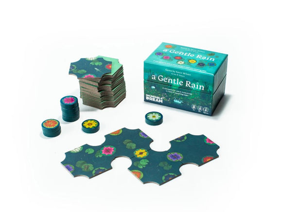 A Gentle Rain - cozy edition game by INcredible Dream. The image features a beautifully designed box with colorful floral artwork. Several game pieces are shown, including round tokens and connecting puzzle-like pieces, showcasing intricate designs of water lilies and flowers. The game is crafted for a calming and relaxing experience, suitable for one or more players.