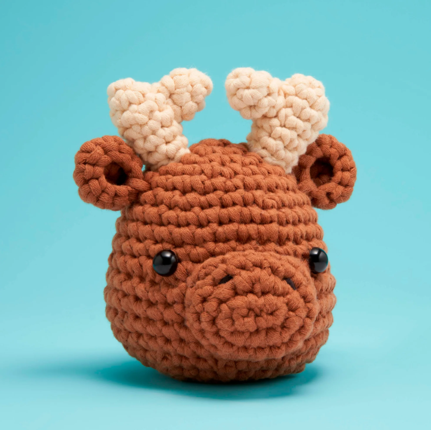 Roosevelt the Moose Beginner C DIY kit by Woobles, featuring a cute, plush moose head crafted from soft yarn in brown and beige colors, with prominent antlers and black safety eyes, set against a bright blue background.