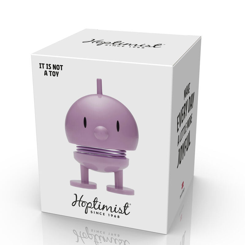 The Hoptimist Bumble S Lavender is a cheerful and whimsical bouncing figure designed to promote joy. The lavender bobblehead features a rounded body, small eyes, and a spring base, packaged in a vibrant white box with the text 'IT IS NOT A TOY' and branding from Hoptimist since 1968, making it a unique decorative item or stress reliever.