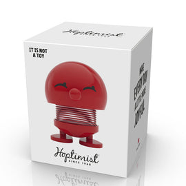 A cheerful red Hoptimist Bimble S figurine, which features a smiling face and a spring base, resting in its packaging, designed to bring joy and positivity.