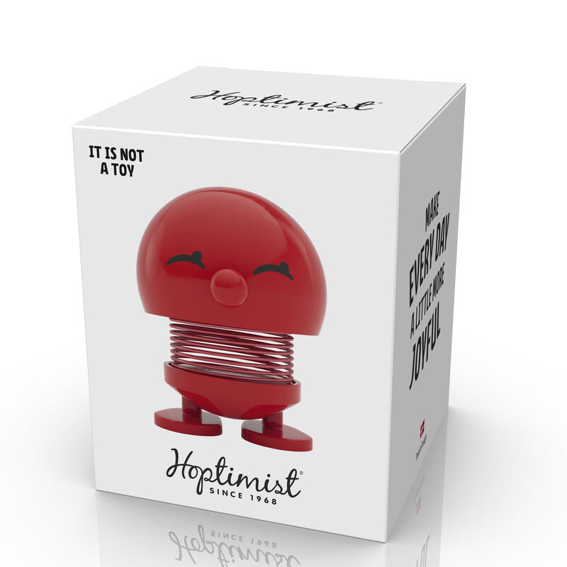 A cheerful red Hoptimist Bimble S figurine, which features a smiling face and a spring base, resting in its packaging, designed to bring joy and positivity.