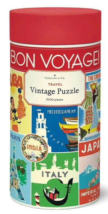 A cylindrical puzzle box labeled 'BON VOYAGE! Travel Vintage Puzzle' with a red lid and a colorful collage of travel-themed illustrations on the label.