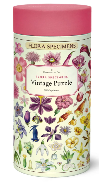 A cylindrical puzzle tin labeled 'Flora Specimens Vintage Puzzle' with a pink lid and a cream-colored body decorated with colorful vintage botanical illustrations. The brand ''Cavallini & Co."