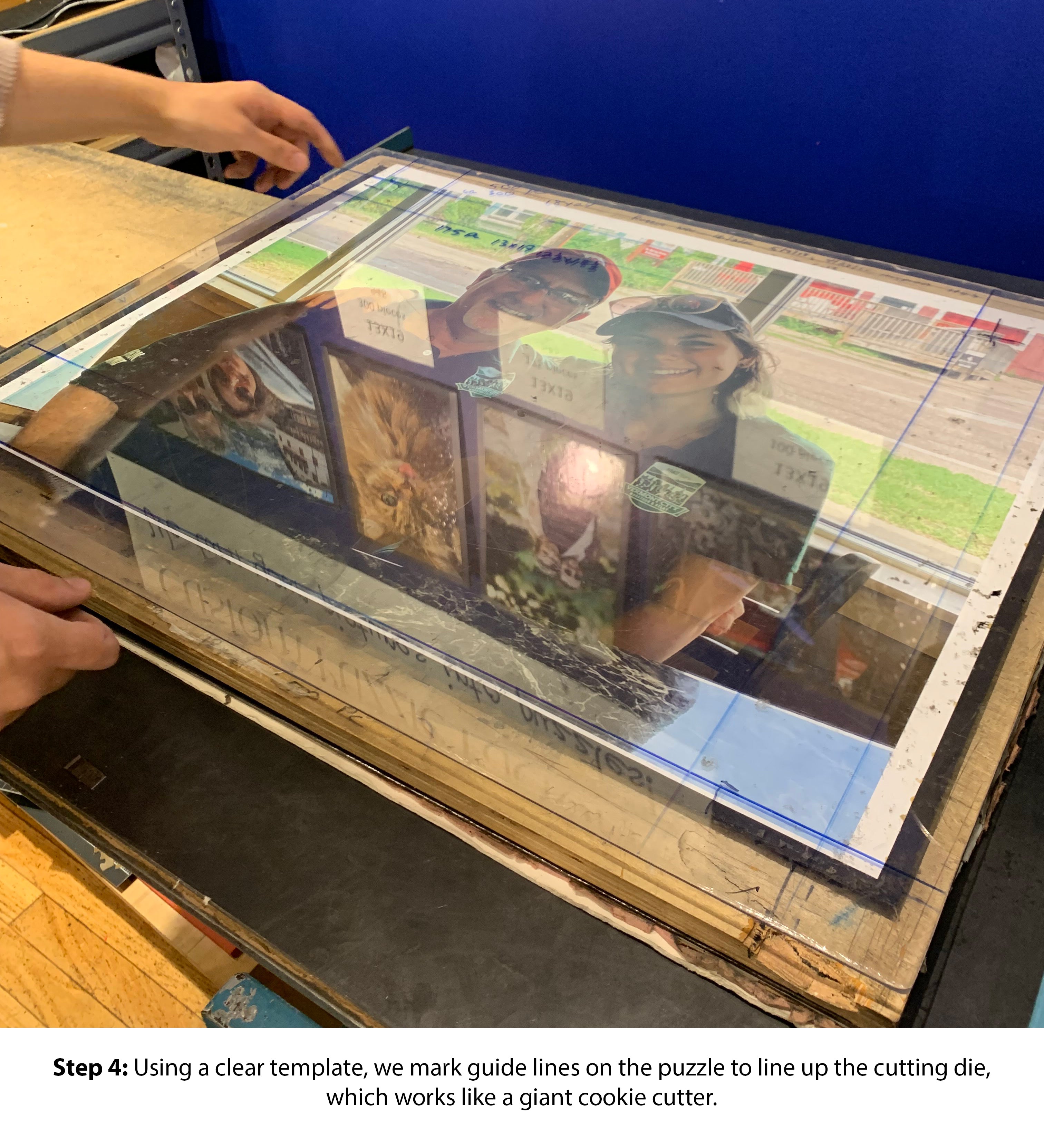 A close-up of hands marking guide lines on a clear template placed over a jigsaw puzzle. The image shows a cutting die being aligned, highlighting the precision involved in creating custom jigsaw puzzles.