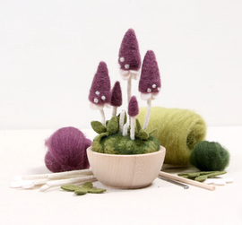 A colorful Pixie Parasol Needle Felting Kit displayed with vibrant, purple felt mushroom figurines atop a round green base surrounded by colorful wool roving and tools. Perfect for crafting enthusiasts!
