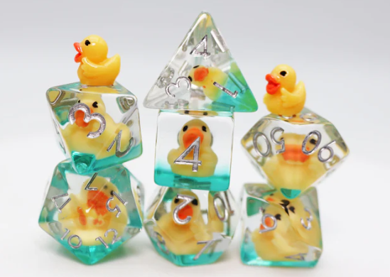 A colorful Rubber Duckie RPG Dice Set featuring whimsical yellow rubber duck figures encapsulated in clear resin dice. The set includes various polyhedral shapes, with the ducks visible within the transparent sides and playful teal accents. Perfect for tabletop gaming enthusiasts who enjoy a fun aesthetic.
